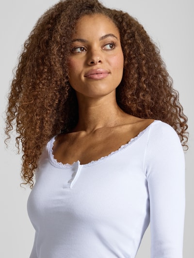 Vrouwenmodel draagt wit shirt met lange mouwen in riblook met kant en knoopsluiting, Model 'MAYA' van NOISY MAY®, mix van katoen en elastaan, slim fit, ruglengte maat S 51 cm, detailopname bovenlichaam.