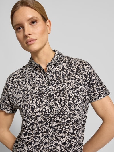 Frauenmodel trägt Relaxed Fit Poloshirt aus reiner Baumwolle von Marc O'Polo, Optik:Allover-Muster, florales Muster, Polokragen, V-Ausschnitt, kurze Knopfleiste, Ärmelform: Kurzarm, Materialverarbeitung: Jersey, Farbe Schwarz mit hellem Florales-Allover-Muster, Nahaufnahme Oberkörper.