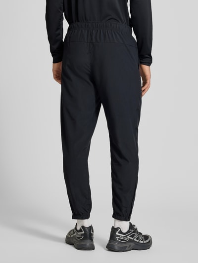 Męskki model trägt Form Pants mit Logo-Print und wpuszczane kieszenie von NIKE TRAINING, dopasowany krój, elastyczny pas, elastyczne zakończenia nogawek, czarny kolor, matowa tekstura, Ganzkörperansicht Rückansicht.