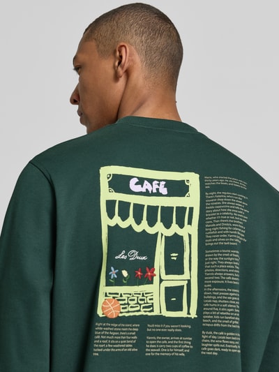 Männermodel trägt Sweatshirt mit Label-Details und Rundhalsausschnitt von Les Deux, Baumwoll-Elasthan-Mix, Regular-Fit, Rückenlänge 66 cm, Ärmellänge 70 cm, dunkelgrün mit Grafikprint, Nahaufnahme Oberkörper Rückansicht.