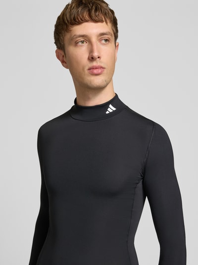 Männermodel trägt schwarzes Sport-Langarmshirt mit Mock-Neck von adidas Training, glatte Textur, Nahaufnahme Oberkörper.