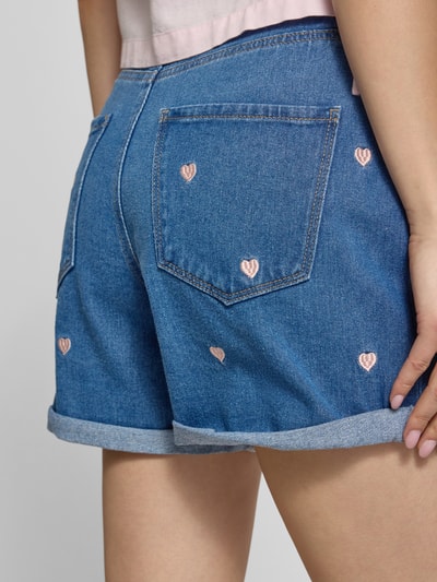 Frauenmodel trägt High Waist Jeansshorts aus reiner Baumwolle Modell 'VEGA' von Only in Denim-Optik mit Stickerei, Kontrastnähten, 5-Pocket-Design, Bundabschluss mit Umschlag, Detailaufnahme Rückansicht.