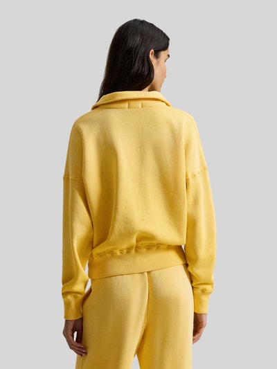 Vrouwenmodel draagt 'Sweatshirt mit Label-Stitching' van Polo Ralph Lauren in geel, katoenmix, losse pasvorm, geribde boorden, rugaanzicht.
