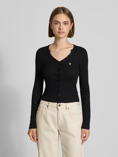 Frauenmodel trägt Slim Fit Longsleeve aus mieszanka bawełny od GUESS, czarny kolor, listwa guzikowa, wyhaftowane logo, długość tyłu w rozmiarze S: 44 cm, Ganzkörperansicht von vorne.