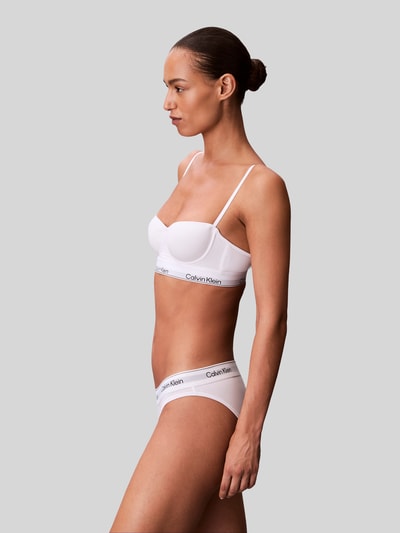 Frauenmodel trägt Balconette BH mit Logo-Stitching von Calvin Klein Underwear in Weiß, Baumwoll-Mix mit Modal-Anteil, Verstellbare Träger, Haken-Verschluss, Ganzkörperansicht von der Seite.