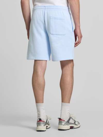 Männermodel trägt Relaxed Fit Sweatshorts aus Baumwoll-Mix von Lacoste in Hellblau, lockere Passform, Struktur weich, Ganzkörperansicht Rückansicht. Herren Sweatshorts von Lacoste.