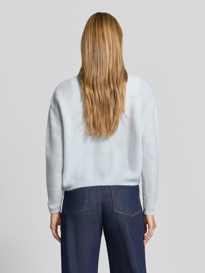 Frauenmodel trägt Relaxed Fit Strickjacke aus Woll-Mix mit Leinen-Anteil von American Vintage, hellblaue Farbe, gerippte Bündchen, Langarm, lockere Passform, Jeans kombiniert, Rückenansicht, Ganzkörperansicht Rückansicht.