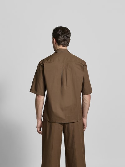 Männermodel trägt Relaxed Fit Freizeithemd mit Kentkragen von Officine Générale in Braun, reine Baumwolle, Ganzkörperansicht Rückansicht. Rückenlänge bei Größe M: 74 cm, Schulterbreite: 60 cm, Ärmellänge: 33 cm, Knopfleiste, Halbarm.
