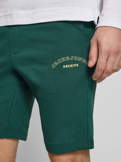 Männermodel trägt Shorts mit Logo-Print Modell 'GORDON' von Jack & Jones aus grünem Baumwoll-Mix mit Relaxed-Fit und Kordelzug, Nahaufnahme Oberschenkelbereich.