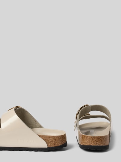 Produktfoto, Hausschuhe aus echtem Leder Modell 'Arizona' von Birkenstock in Beige mit Zierschnalle, abgerundete Passform, Absatzhöhe 3 cm, Schaftweite 7 cm, strukturierte Oberfläche, Detailansicht der Sohle und Seitenpartie