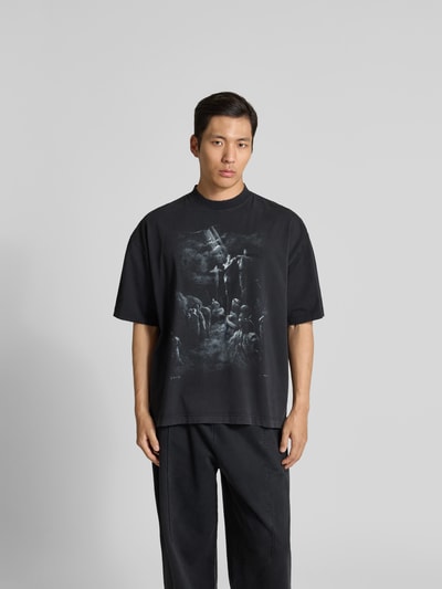 Männermodel trägt Relaxed Fit T-Shirt aus Baumwolle von VETEMENTS in Schwarz mit Destroyed-Look und Motiv-Print, Ganzkörperansicht von vorne.