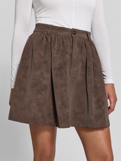 Frauenmodel trägt Minirock aus Viskose-Mix Modell 'Shea' von BAUM & PFERDGARTEN in Braun, A-Linie mit Falten-Optik, Nahaufnahme Oberkörper.