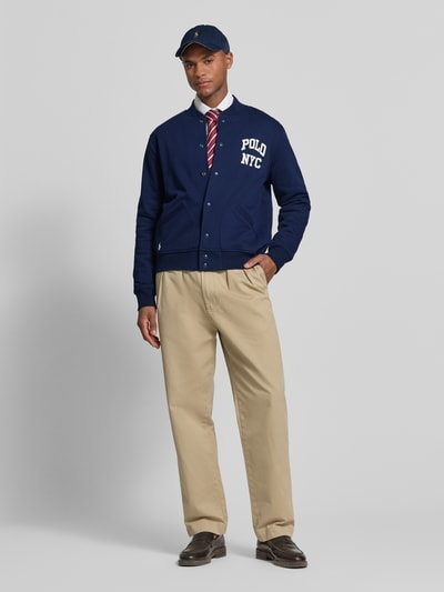 Männermodel trägt Regular Fit College-Jacke aus Baumwoll-Mix von Polo Ralph Lauren, Optik: Unifarben, Schriftzug, Langarm, seitliche Eingrifftaschen, College-Kragen, Verschluss: Druckknöpfe, Material: Baumwoll-Mix, Ganzkörperansicht von vorne.