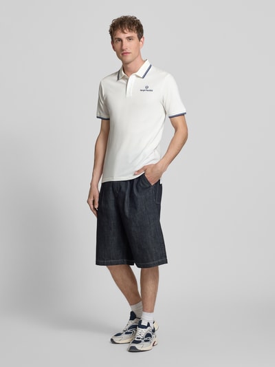 Männermodel trägt Slim Fit Poloshirt mit Logo-Stitching Modell 'Reed' von SERGIO TACCHINI, weiß-blau, elastischer Baumwoll-Mix, Ganzkörperansicht von vorne.