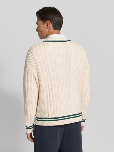 Männermodel trägt Strickpullover mit Zopfmuster von REVIEW, cremefarben mit grünen Kontraststreifen, Ganzkörperansicht Rückansicht.