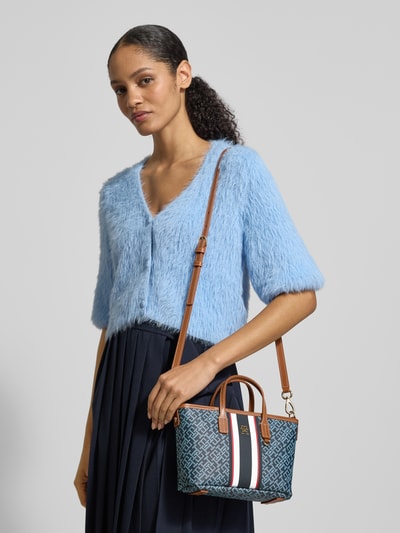 Kobiece modelka trägt Henkeltasche in Lederoptik von Tommy Hilfiger z niebieskim allover-motywem, brązowe uchwyty, odpinany pasek, zamknięcie na zamek, główna komora, Ganzkörperansicht von vorne.
