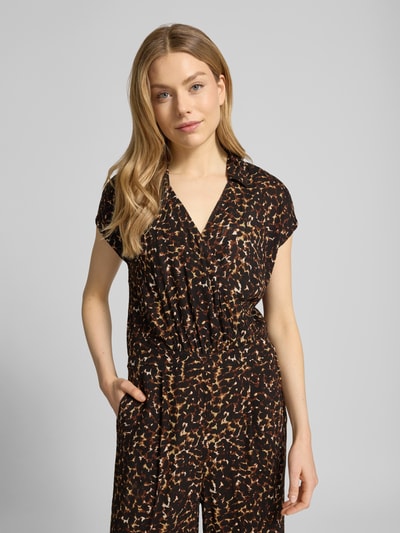 Modelka kobieca nosi Jumpsuit aus Viskose Modell 'MARRAKECH' od ICHI, czarny wzór allover, krój regular fit, szerokość w rozmiarze S 47 cm, długość całkowita w rozmiarze S 136 cm, długość nogawki wewnętrznej w rozmiarze S 68 cm, kołnierzyk, dekolt V, przód w półzbliżeniu.