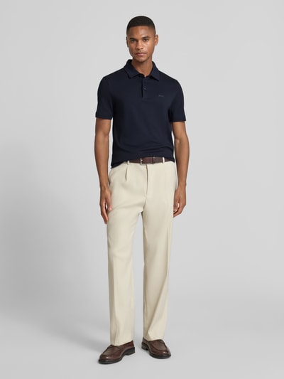 Männermodel trägt Poloshirt mit Brand-Schriftzug von BOSS aus reiner Baumwolle, Regular-Fit, in Dunkelblau, Ganzkörperansicht von vorne.