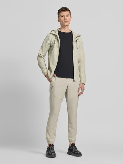 Mannenmodel draagt Regular Fit Jogger met Logo-Print model 'Vibe' van Under Armour, beige kleur, elastische stof, zijzakken, elastische tailleband met trekkoord, elastische boorden, regular fit, productcontext: heren jogger, volledige lichaamsaanzicht van voren.