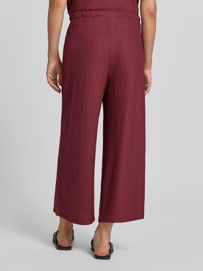 Frauenmodel trägt Loose Fit Hose in Crinkle-Optik von s.Oliver RED LABEL in Dunkelrot mit strukturierter Oberfläche, Ganzkörperansicht Rückansicht.