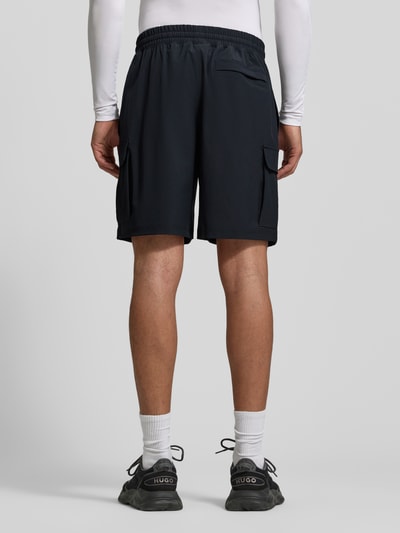 Männermodel trägt Straight Fit Shorts mit Cargo-Taschen Modell 'Vibe' von Under Armour, Schwarz, elastischer Bund, Ganzkörperansicht Rückansicht.
