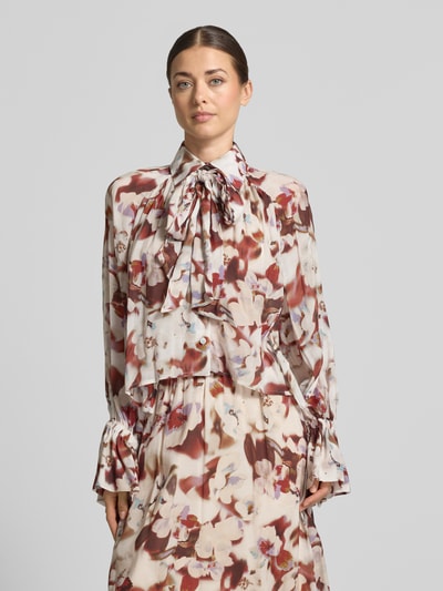 Frauenmodel trägt Bluse mit Schleife Modell 'VAELIE' von DRYKORN, cremefarben mit floralem Muster, Material-Mix, Nahaufnahme Oberkörper.