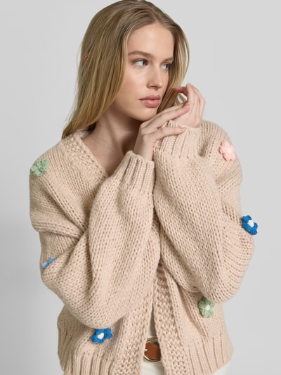 Frauenmodel trägt Oversized Strickjacke mit floralem Zierbesatz von Apricot, Grobstrick, offene Vorderseite, Nahaufnahme Oberkörper.