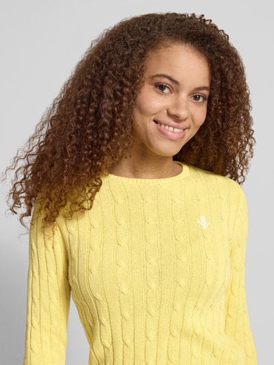 Frauenmodel trägt Strickpullover mit Zopfmuster und Label-Stitching von REVIEW in Gelb, aus Baumwoll-Mix, Regular-Fit, Nahaufnahme Oberkörper.