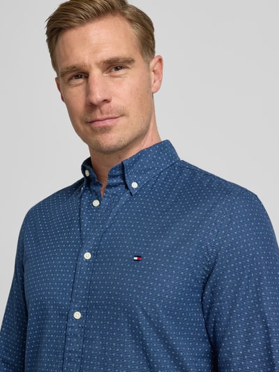 Męską model nosi Slim Fit Freizeithemd aus reiner Baumwolle od Tommy Hilfiger, niebieska popelina z nadrukiem, zbliżenie na górę ciała.