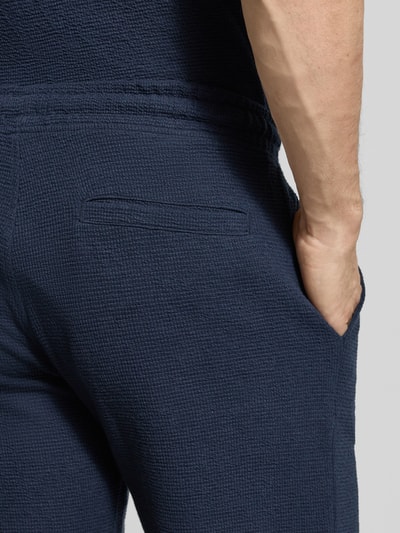 Männermodel trägt Sweatshorts mit elastischem Bund von MCNEAL in Blau mit Strukturmuster, Gesäßtasche, Elastischer-Material-Mix, Nahaufnahme Rückansicht.