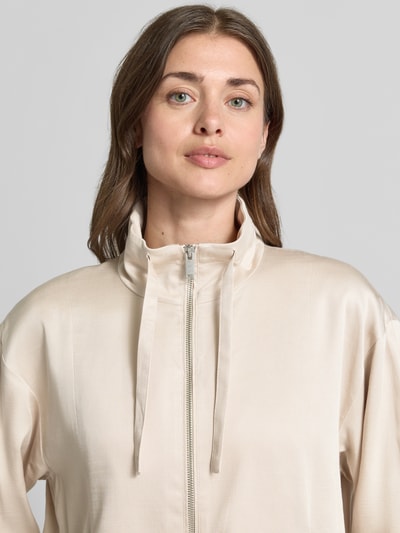 Frauenmodel trägt Jacke aus Lyocell-Baumwoll-Mix Modell 'Jarusa' von OPUS in Beige mit Stehkragen, Reißverschluss, Nahaufnahme Oberkörper. Rückenlänge bei Größe 36: 56 cm, Schulterbreite: 54 cm, Brustweite: 57 cm, Ärmellänge: 53 cm, Relaxed-Fit.