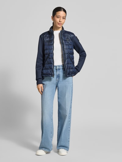 Frauenmodel trägt Steppjacke mit Label-Patches Modell 'HASKEL' von Blauer Usa in Dunkelblau, kombiniert mit geradem Schnitt, Stehkragen, Zweiwege-Reißverschluss, seitlichen Reißverschlusstaschen, strukturierte Oberfläche; Ganzkörperansicht von vorne.