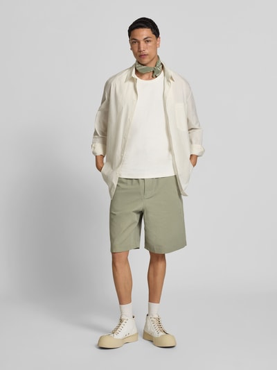 Männermodel trägt Shorts aus Baumwoll-Mix von MAISON KITSUNÉ in Grün mit elastischem Bund, Eingrifftaschen, Regular-Fit, Knielänge, Ganzkörperansicht von vorne.