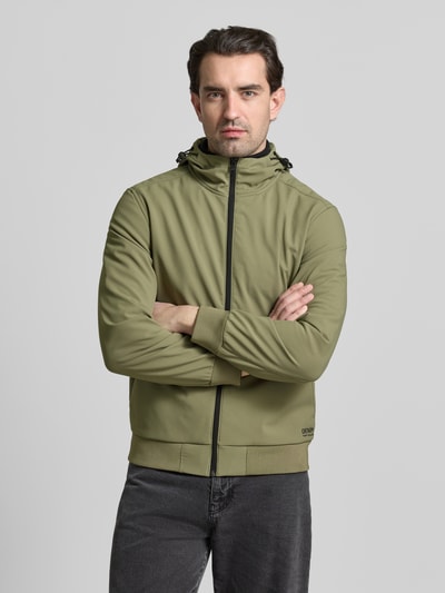 Männermodel trägt Regular Fit Funktionsjacke mit Kapuze von Tom Tailor Denim in Olivgrün, unifarben, langarm, elastische Abschlüsse, ganzkörperansicht von vorne. Die Jacke ist wasserdicht, atmungsaktiv und wärmeisolierend, mit Stehkragen, Tunnelzug und Label Stitching.
