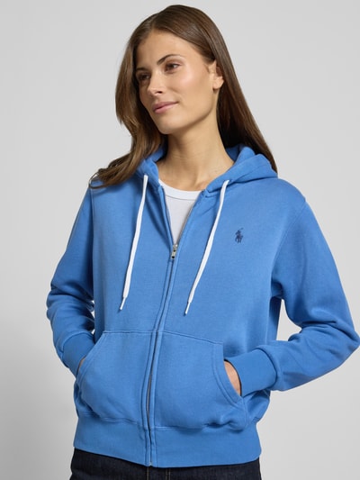 Kobiece model prezentuje bluzę rozpinaną z kapturem od Polo Ralph Lauren, mieszanka bawełny, luźny krój, wpuszczane kieszenie, wyhaftowane logo, prążkowane wykończenia. Ujęcie: zbliżenie na górną część ciała z przodu.