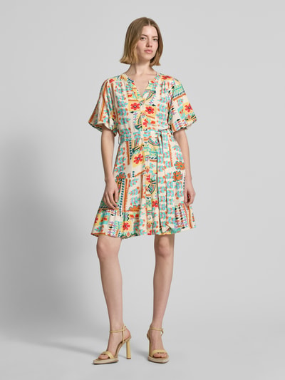 Kobiece modelka nosi sukienkę mini z mieszanki wiskozy i lnu Minikleid aus Viskose-Mix mit Leinen-Anteil von Apricot, taliowany krój, kwiatowy nadruk na całej powierzchni, listwa guzikowa, rękaw o dł. 1/2, odpinana materiałowa tasiemka, dekolt z lamówką, długość tyłu w rozmiarze S: 85 cm, szerokość w rozmiarze S: 52 cm, długość rękawów w rozmiarze S: 28 cm, wielokolorowe wzory, miękka tekstura, cała sylwetka z przodu.