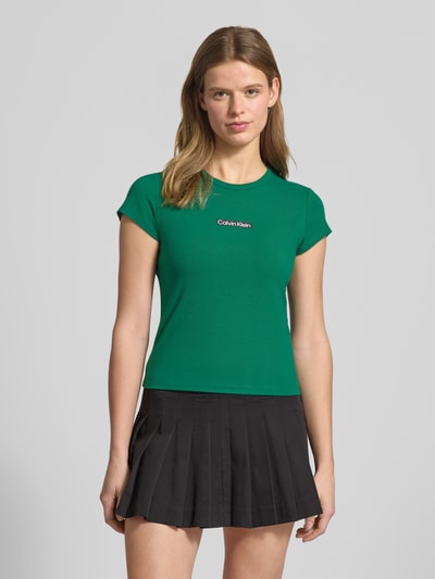 Kobiece modelka nosi T-shirt mit Rundhalsausschnitt und Label-Print von Calvin Klein Jeans, krój slim fit, mieszanka bawełny i elastanu, okrągły dekolt, nadruk z logo, długość tyłu w rozmiarze S: 42 cm, kolor zielony, widok całej sylwetki z przodu.