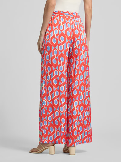 Frauenmodel trägt Stoffhose aus reiner Viskose von Milano Italy mit rot-blauem Muster, weitem Bein, elastischem Bund, Ganzkörperansicht Rückansicht.