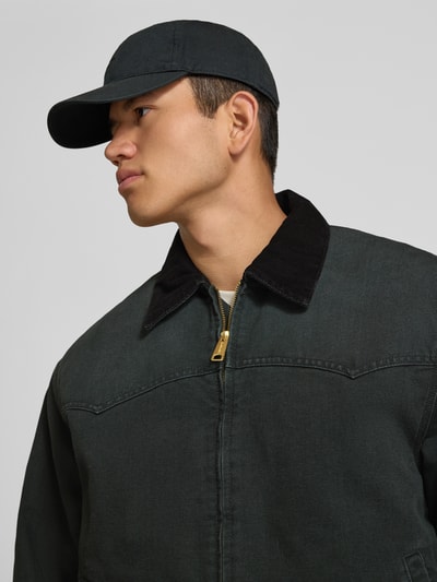 Männermodel trägt Jacke mit Reißverschluss und Label-Detail Modell 'Santa Fe' von Carhartt Work In Progress aus Baumwolle in Dunkelgrün, Nahaufnahme Oberkörper.