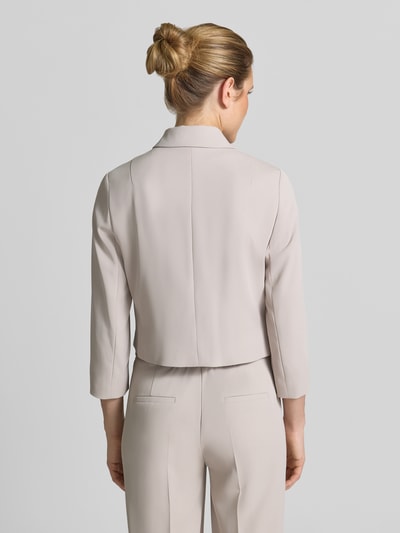 Kobieta modelka ma na sobie Regular Fit Blazer mit Umlegekragen od Betty Barclay w jasnobeżowym kolorze, faktura gładka, garniturowy materiał; elastyczna mieszanka materiałów, patki kieszeniowe, pełna linia guzików, taliowany krój, długość tyłu w rozmiarze 36: 49 cm, szerokość w rozmiarze 36: 47 cm, długość rękawa w rozmiarze 36: 52 cm; widok całopostaciowy z tyłu.