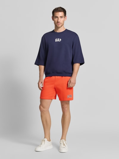 Mannenmodel draagt Straight fit korte broek met gestikt logo Model 'Heritage' van GAP in katoenmix, oranje, band met tunnelkoord, ganzekörpervooraanzicht.