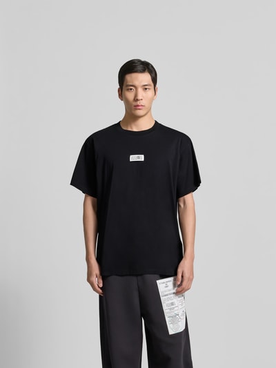 Männermodel trägt Relaxed Fit T-Shirt mit Logo-Detail von MM6 Maison Margiela in Schwarz, reine Baumwolle, Rundhalsausschnitt, Ganzkörperansicht von vorne.