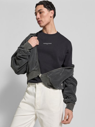Männermodel trägt Regular Fit T-Shirt aus Baumwolle von MAISON KITSUNÉ, schwarz, Rundhalsausschnitt, Label-Stitching, Nahaufnahme Oberkörper.