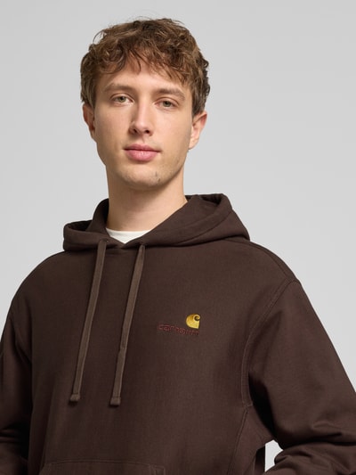 Männermodel trägt Hoodie mit Kapuze von Carhartt Work In Progress in Braun, Baumwoll-Mix, Lockerer-Schnitt, Label-Stitching, Nahaufnahme Oberkörper.