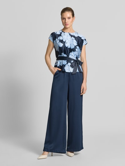 Vrouwenmodel draagt Loose Fit Pants met elastische tailleband en steekzakken van Christian Berg Cocktail in donkerblauw met lichte glans, vloeiende stof, french pockets, rechte wijde pijpen, full body vooraanzicht.