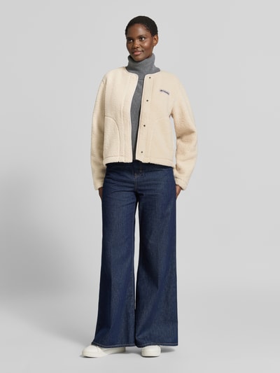 Frauenmodel trägt Jacke mit Label-Patch Modell 'Panorama' von Columbia, Polar, krój straight fit, okrągły dekolt, zapięcie na zatrzask, naszywka z logo, wpuszczane kieszenie, długość tyłu w rozmiarze S: 55 cm, szerokość ramion w rozmiarze S: 44 cm, szerokość w rozmiarze S: 50 cm, długość rękawów w rozmiarze S: 62 cm, jasny beż, granatowe spodnie, gładkie tekstury, Ganzkörperansicht von vorne
