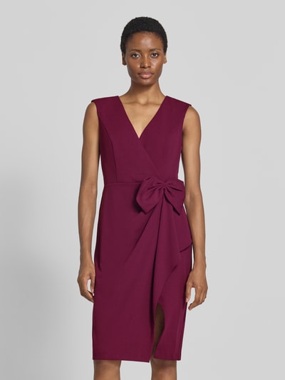 Frauenmodel trägt Knielanges Kleid mit Zierschleife von Adrianna Papell in Bordeaux, ärmellos, V-Ausschnitt, Ganzkörperansicht von vorne, taillierte Passform, Wickel-Optik, elastischer Material-Mix, Zierschleife und Raffungen, mittellange Länge.