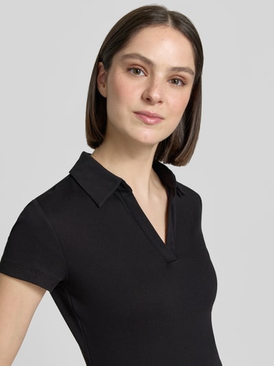 Frauenmodel trägt schwarzes T-Shirt mit Polokragen Modell 'Kleoh Polo' von Someday aus Baumwoll-Elasthan-Mix in Ripp-Optik, Nahaufnahme Oberkörper.