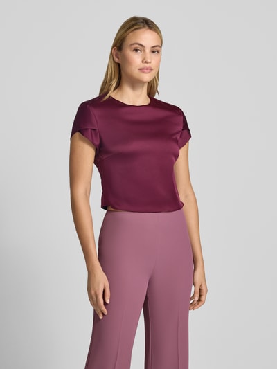 Frauenmodel trägt Bluse aus Satin von Rinascimento in Dunkelviolett mit glänzender Oberfläche, gerade Passform, Nahaufnahme Oberkörper. Material-Mix mit Stretch-Anteil, Rundhalsausschnitt, kurzärmelig, rückseitiger Knopfverschluss, Rückenlänge bei Größe S: 44 cm.