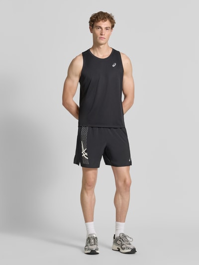 Męski model nosi Regular Fit Shorts mit integriertem Slip Modell 'ICON' od ASICS TIGER, czarne z nadrukiem z logo, elastyczny pas, szerokość w rozmiarze M: 37 cm, długość wewnętrzna nogawki w rozmiarze M: 18 cm, krój regular fit, całkowity widok z przodu